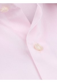 Lichtroze shirt met een gestructureerde stof, een kleine kraag en een enkele knoopsluiting in de linkerbovenhoek.