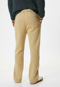 Beige sweatpants med en afslappet pasform, featuring en elastisk talje, baglomme og tapered ben med ribbede manchetter. Glat tekstur.
