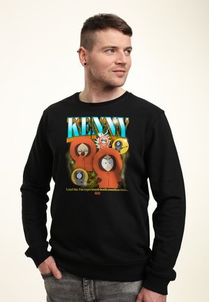Mand iført sort sweatshirt med farverig South Park-figur Kenny og tekst om at opleve døden utallige gange, hænderne i lommerne.