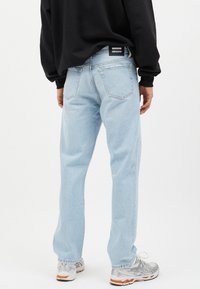 Jeans de denim azul claro con corte holgado, cinco bolsillos y una etiqueta de marca negra en la parte trasera. Combinados con zapatillas grises y naranjas.
