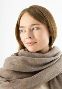 Écharpe douce de couleur marron enroulée autour du cou, en tissu tricoté, présentant une texture lisse et un design volumineux.