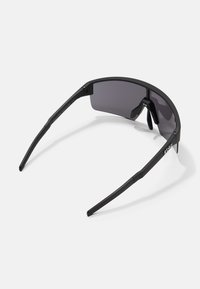 Gafas de sol deportivas negras con un diseño angular elegante, lentes oscuros y acentos de goma negra texturizada en las patillas.