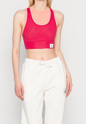 Pink mesh sports crop top with wide straps, layered over a light peach base layer. Paired with white jogger pants featuring logo patch.
