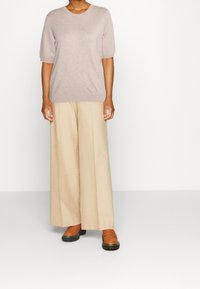 Beige korte mouw gebreid topje gecombineerd met beige wijde broek en bruine instappers met een textuurrijke zool. Minimalistisch ontwerp, zachte stof.