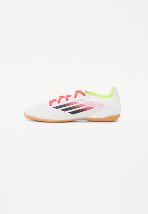 Scarpe da ginnastica bianche con lacci rosa, logo nero e rosso, tomaia testurizzata, suola arancione e dettagli verde lime sul tallone e sulla linguetta.