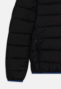 Giacca a vento nera con design trapuntato, superficie leggermente lucida, polsini elasticizzati con accenti blu e tasca laterale con zip.