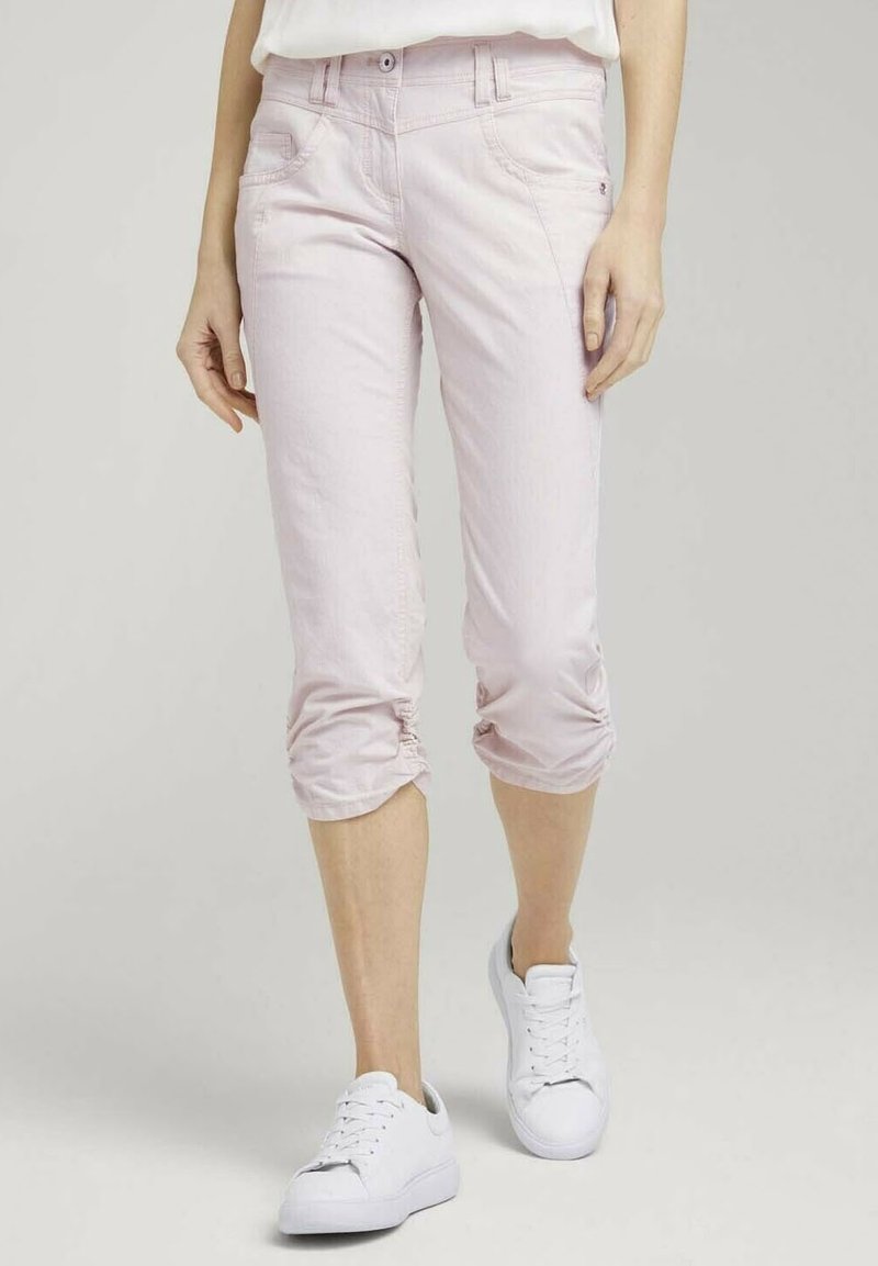Jasnoróżowe spodenki capri wykonane z denimu, charakteryzujące się dopasowanym fasonem, przednimi kieszeniami i marszczonymi mankietami, połączone z białymi trampkami.
