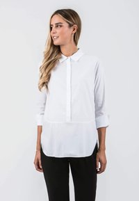 White long-sleeve shirt with a buttoned collar, a front placket, and a straight cut, featuring rolled-up sleeves and side slits.
