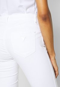 Witte spijkerbroek van denim met een aansluitende pasvorm, een achterzak met een driehoekig reliëflogo en een gladde textuur. Geen zichtbare slijtageplekken.