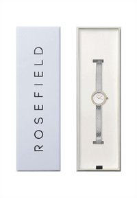 Montre-bracelet en mailles argentées avec un cadran rond blanc, des accents dorés et des embellissements en cristal, présentée dans une boîte bleu clair.