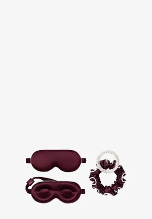 Dos antifaces de seda burdeos para dormir y dos coleteros a juego, uno burdeos y uno blanco, sobre un fondo blanco.
