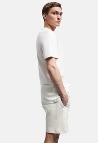 Crème-kleurig katoenen t-shirt met korte mouwen en een relaxte pasvorm, gecombineerd met bijpassende knielange shorts, beide met een gladde textuur.