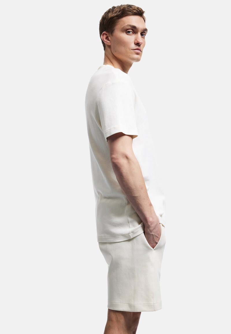 Crème-kleurig katoenen t-shirt met korte mouwen en een relaxte pasvorm, gecombineerd met bijpassende knielange shorts, beide met een gladde textuur.