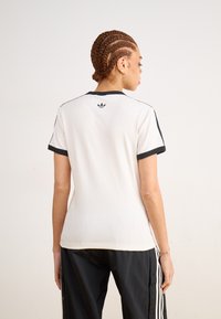 Hvit atletisk t-skjorte med svarte detaljer, korte ermer og rund hals. Har en liten logo på øvre rygg. Glatt tekstur.