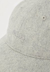 Boné cinzento em feltro com a palavra "BOSS" bordada em fio cinzento. Apresenta uma copa estruturada e aba curva, com orifícios de ventilação nas laterais.