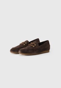 Une paire de mocassins en daim marron avec des lacets beige et des semelles en caoutchouc sur un fond blanc uni.