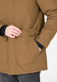 Brun isolerad parka med dragkedja fram, fickor med lappar och kardborreknäppning, med en slät yta och en figurnära passform.