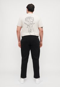 White t-shirt with a black line drawing of a flower and hand on the back, paired with black pants and white sneakers.