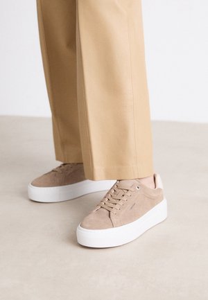 Zapatillas deportivas de plataforma de ante beige con suelas blancas gruesas, combinadas con pantalones beige de pierna ancha a juego.
