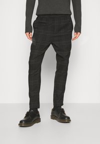 Zwarte geruite broek met een elastische tailleband, taps toelopende pijpen en een gestructureerde stof, gecombineerd met zwarte veterschoenen.