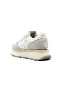 La scarpa presenta una toma in pelle bianca e camoscio grigio, una suola piatta con una striscia grigia chiara e un accent florale sul tallone.
