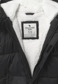 Gilet imbottito nero con un morbido rivestimento interno in pile bianco, dotato di etichetta Abercrombie Kids taglia 11/12, chiusura con zip e due tasche laterali.