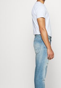 Světle šedé upnuté tričko v kombinaci se světle modrými džíny, které mají slim fit, vybledlou texturu a opotřebované detaily na stehnech.