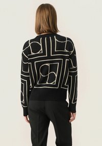 Sweter dzianinowy w kolorze czarnym z białymi wzorami geometrycznymi; ma okrągły dekolt, prążkowane mankiety i dół, a także luźny krój.