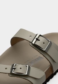 Ανοιχτό μπεζ σανδάλι με δύο ρυθμιζόμενους ιμάντες, ασημένιες αγκράφες και μαλακό πέλμα. Διαθέτει υφασμένο λάστιχο σόλας για πρόσφυση.