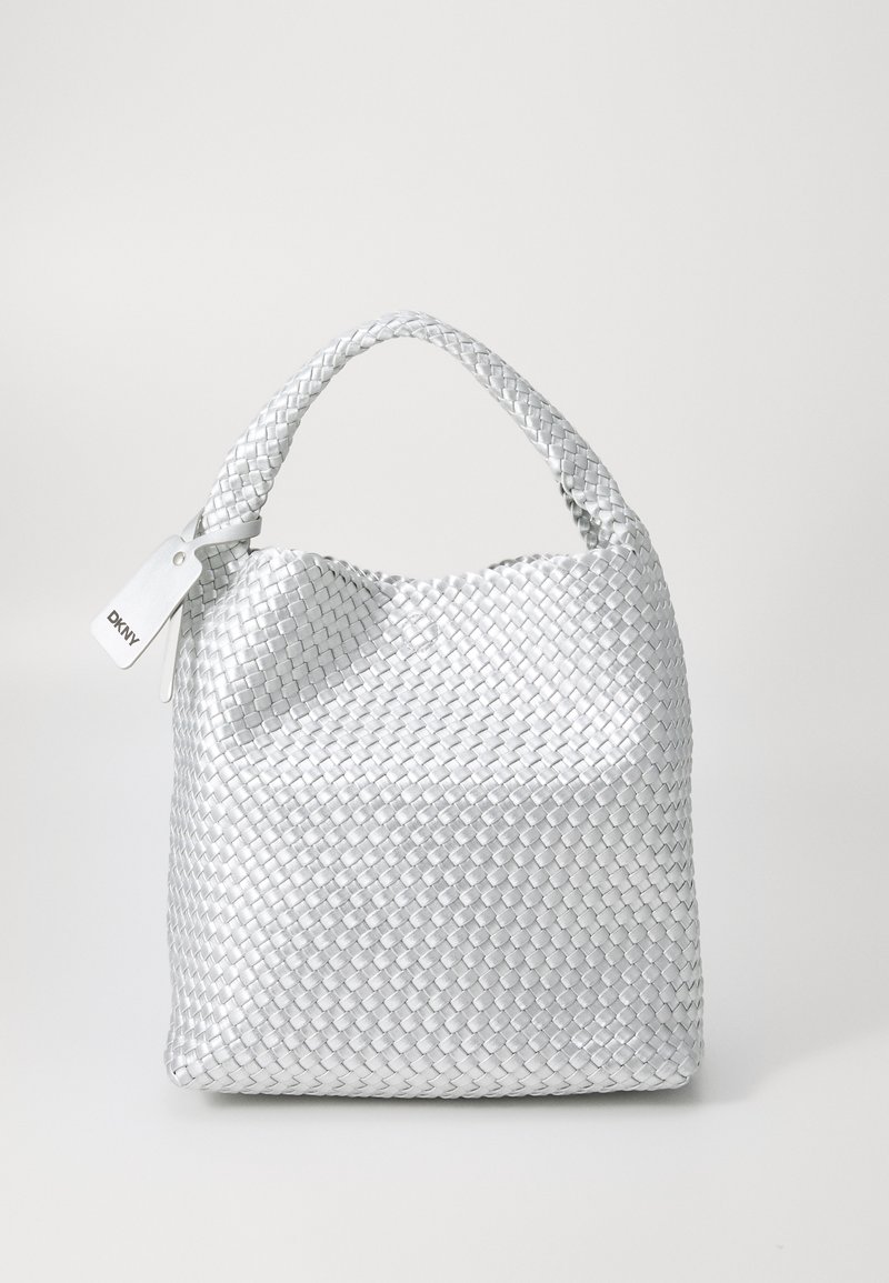 Πλεκτή ασημένια τσάντα με στρογγυλό σχήμα, υφασμάτινη επιφάνεια και κοντό χερούλι. Διαθέτει μια λευκή ετικέτα με το λογότυπο.
