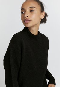 Schwarzer Strickpullover mit hohem Kragen, lockerer Passform und langen Ärmeln. Weicher Stoff mit leichtem Glanz, der ein minimalistisches Design zur Schau stellt.