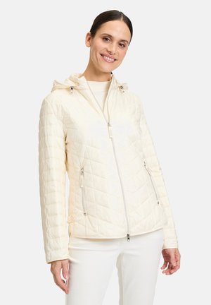 Quilted cream jacket with a zip front, adjustable hood, and metallic hardware. Features side pockets and a smooth, glossy texture.