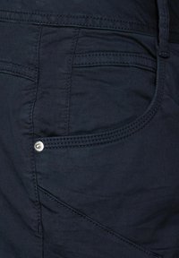 Navyblå tyg av byxor nära, med en ficka med silverfärgad metallknapp, synlig sömnad och texturerad finish.