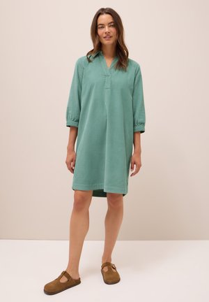Teal katoenen jurk met een relaxte pasvorm, driekwartmouwen en een V-halslijn, gecombineerd met bruine suède klompen. Soepele textuur, eenvoudig ontwerp.