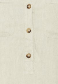 Ljust beige knapp-up skjorta gjord av texturerat tyg, med fem runda bruna knappar och en bröstficka på vänster sida.