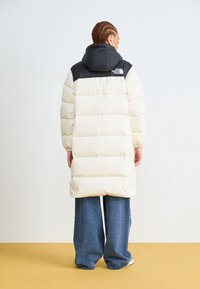 Witte en zwarte pufferjack met een capuchon, voorzien van horizontale gestikte secties, elastische manchetten en een logo op de achterkant.