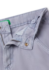 Pantalones de mezclilla de color azul claro con cierre de cremallera, un botón decorativo y una etiqueta de etiqueta verde. La tela tiene un sutil patrón texturizado.