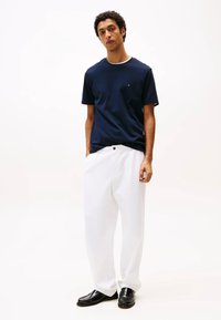 T-shirt blu a maniche corte, pantaloni bianchi morbidi e mocassini neri. La t-shirt presenta un logo discreto sul petto. Tessuto di trama liscia.