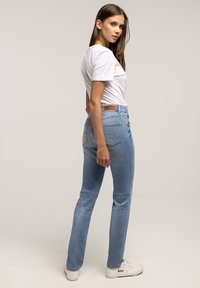 Jasnoniebieskie, proste dżinsy z subtelnym cieniowaniem, pięcioma kieszeniami, jasnymi przeszyciami oraz beżową skórzaną naszywką na tylnej części pasa.