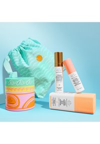 Four Drunk Elephant skincare products and a teal drawstring pouch arranged on a blue background.