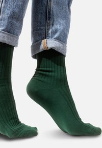Zielone skarpetki z żebrowanej tkaniny, wykonane z miękkiego materiału, z dopasowanym krojem, który przylega do kostki. Widoczna tekstura i subtelne detale szwów.
