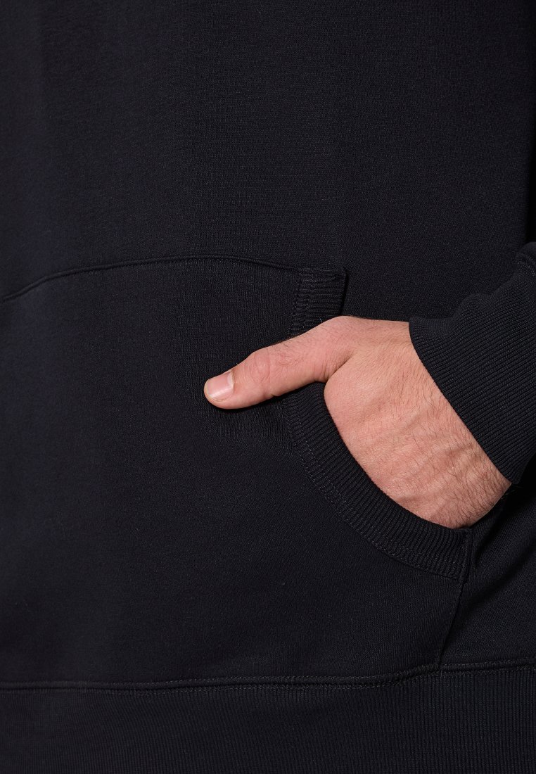 Hand, die in der vorderen Tasche eines schwarzen Sweatshirts ruht, zeigt die Textur des Stoffes und die Nähdetails.
