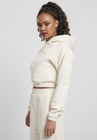 Kremfarget cropped hettegenser med snor i hetten, elastiske mansjetter og matchende høy midje bukser, vist på en modell.