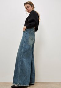 Wijdvallende jeans van lichtblauwe denim, met een hoge taille, voor- en achterzakken, en een uitgerafelde zoom. Gecombineerd met een zwart cropped trui.