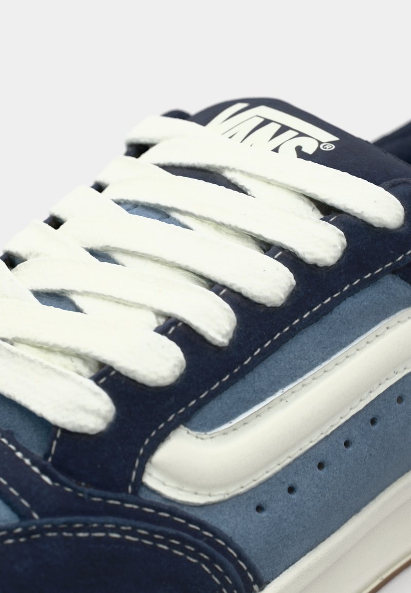 Baskets en daim bleu marine avec des lacets blancs et des accents latéraux. Présente une bande lisse en cuir blanc et des détails de coutures contrastants.