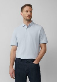 Helles blaues Poloshirt mit klassischem Kragen, kurzen Ärmeln mit aufgerollten Manschetten und einer Dreiknopf-Leiste, kombiniert mit dunklen Jeans.