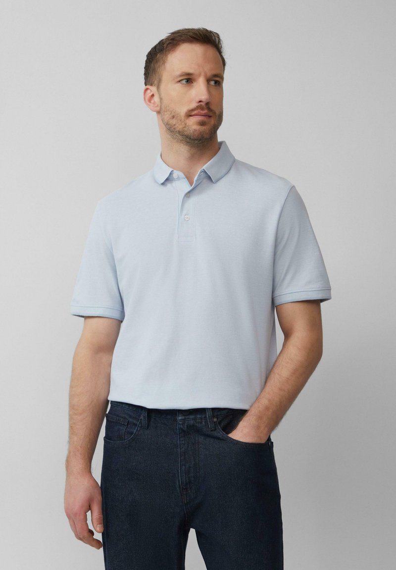 Helles blaues Poloshirt mit klassischem Kragen, kurzen Ärmeln mit aufgerollten Manschetten und einer Dreiknopf-Leiste, kombiniert mit dunklen Jeans.