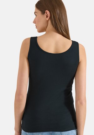 Femme aux longs cheveux bruns portant un haut noir ajusté sans manches et un jean bleu clair, vue de dos sur un fond uni.