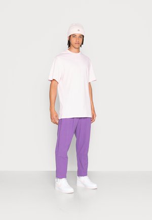 Ljusrosa bomulls-t-shirt, avslappnad passform; lila smalna byxor; vita sneakers med ljusrosa detaljer; bärande en ljusrosa mössa.