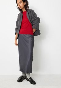 Grå tekstureret jakke over en rød sweater, parret med en slank mørkegrå satin-nederdel og sorte loafers med grå sokker. Simpel, moderne stil.